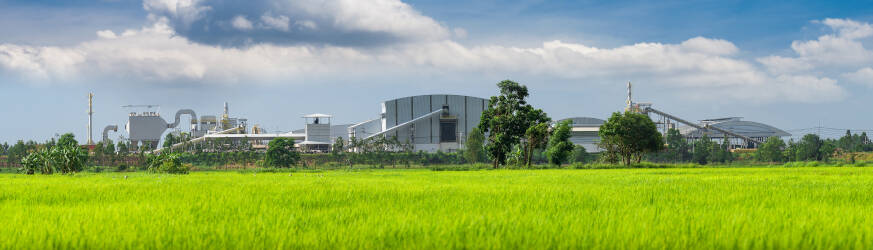 Industrial factory behind a vibrant green field under a clear blue sky
