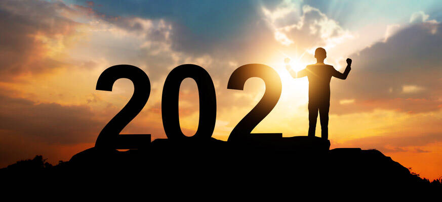 Silhouette of a person standing with arms raised beside the numbers 2021 at sunset